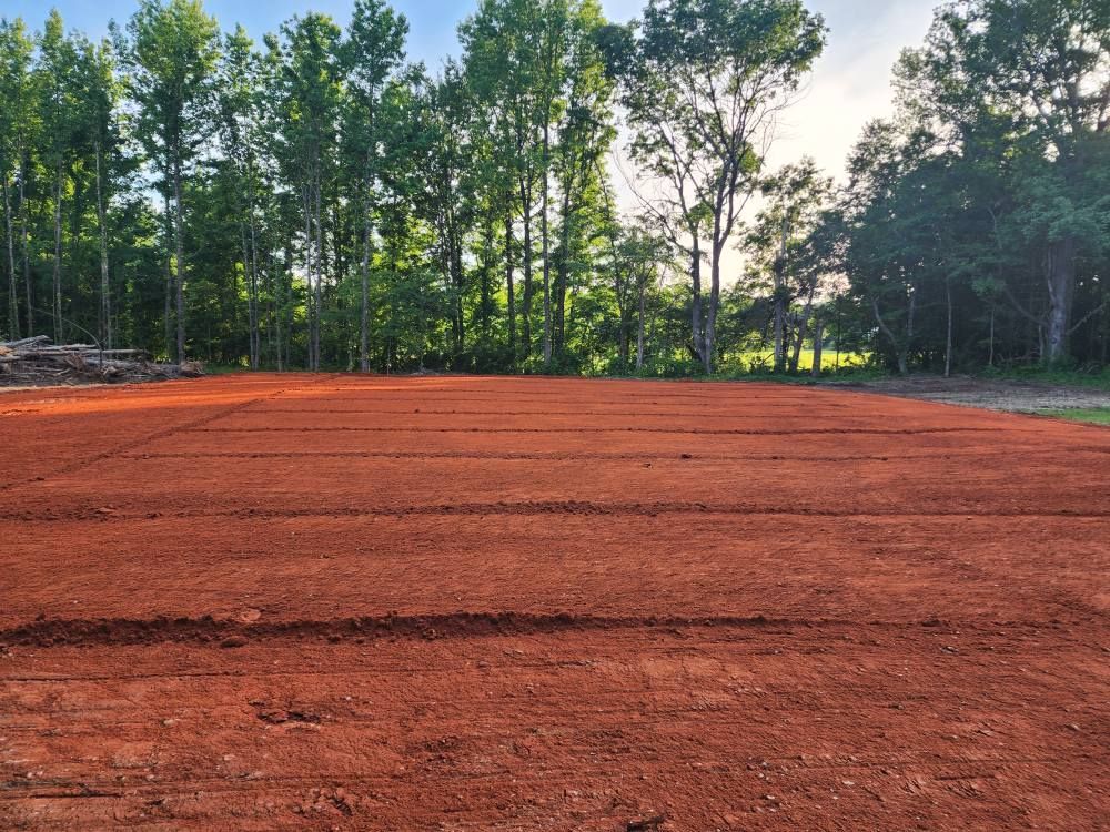 A cleared, red-dirt field, neatly lined, with trees in the background under a bright blue sky.