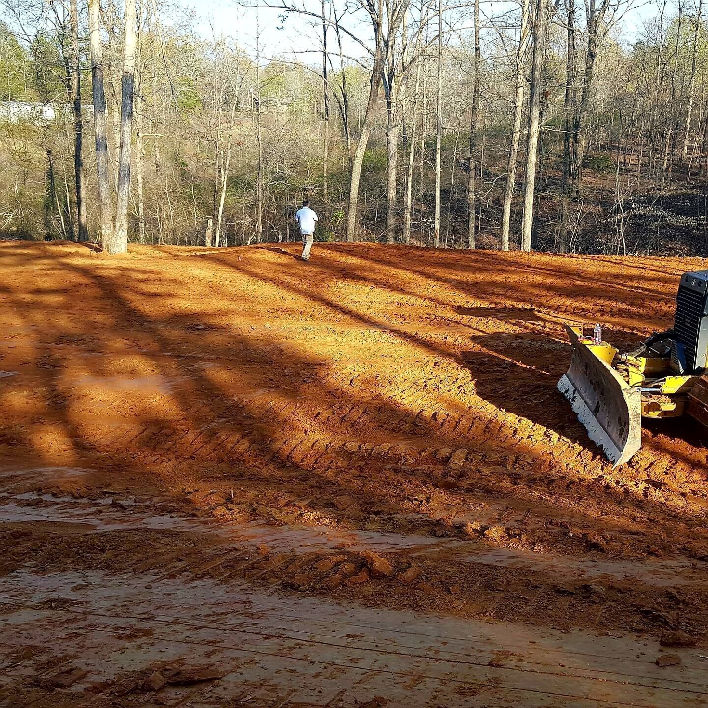 Yellow backhoe on a dirt lot, with trees in the background under a blue sky.
