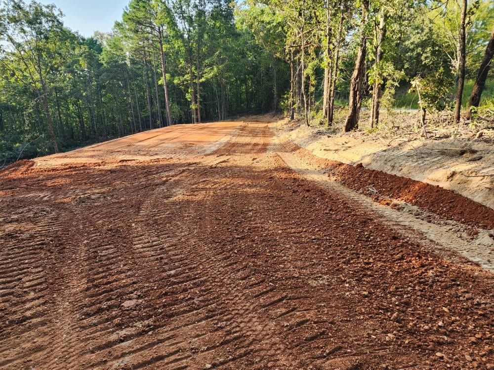 Dirt road through a forest; red soil, tire tracks, trees on either side.