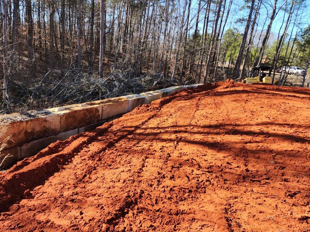 Red dirt area with a stone wall and trees in the background.