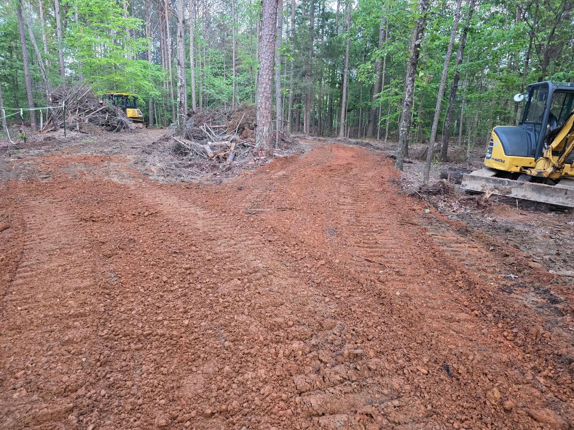 Cleared area in a wooded setting with red soil and heavy equipment, preparing the land.