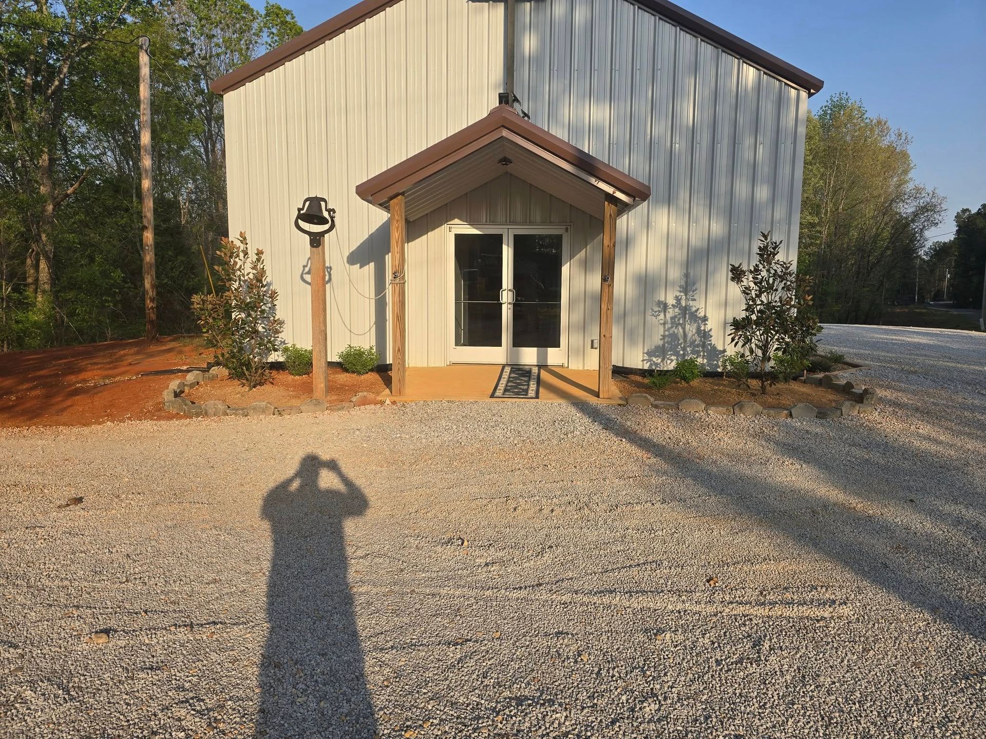 A metal building with a small porch and a gravel driveway, with a person's shadow in the foreground.