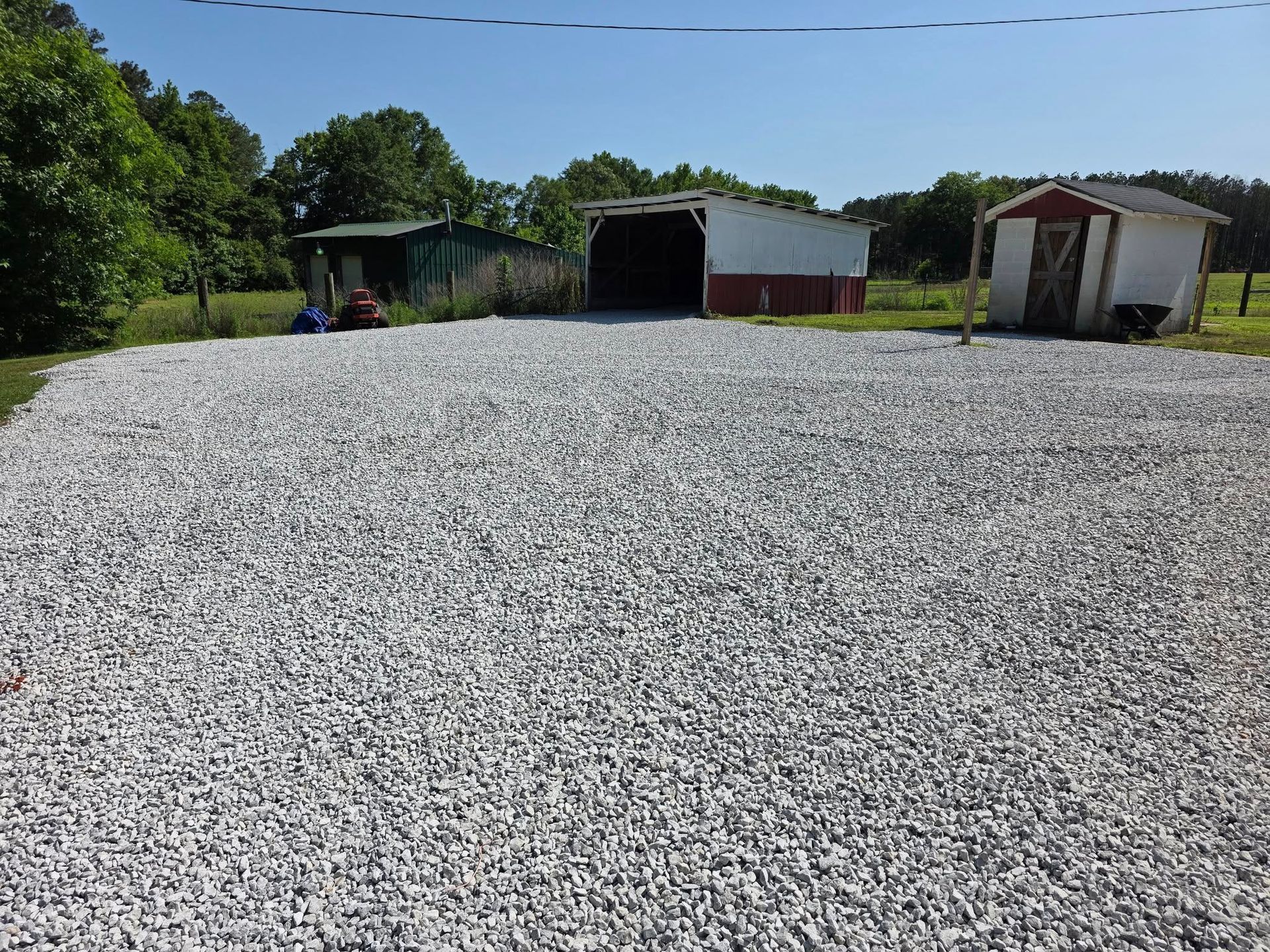 Gravel driveway with three small outbuildings under a clear, blue sky.