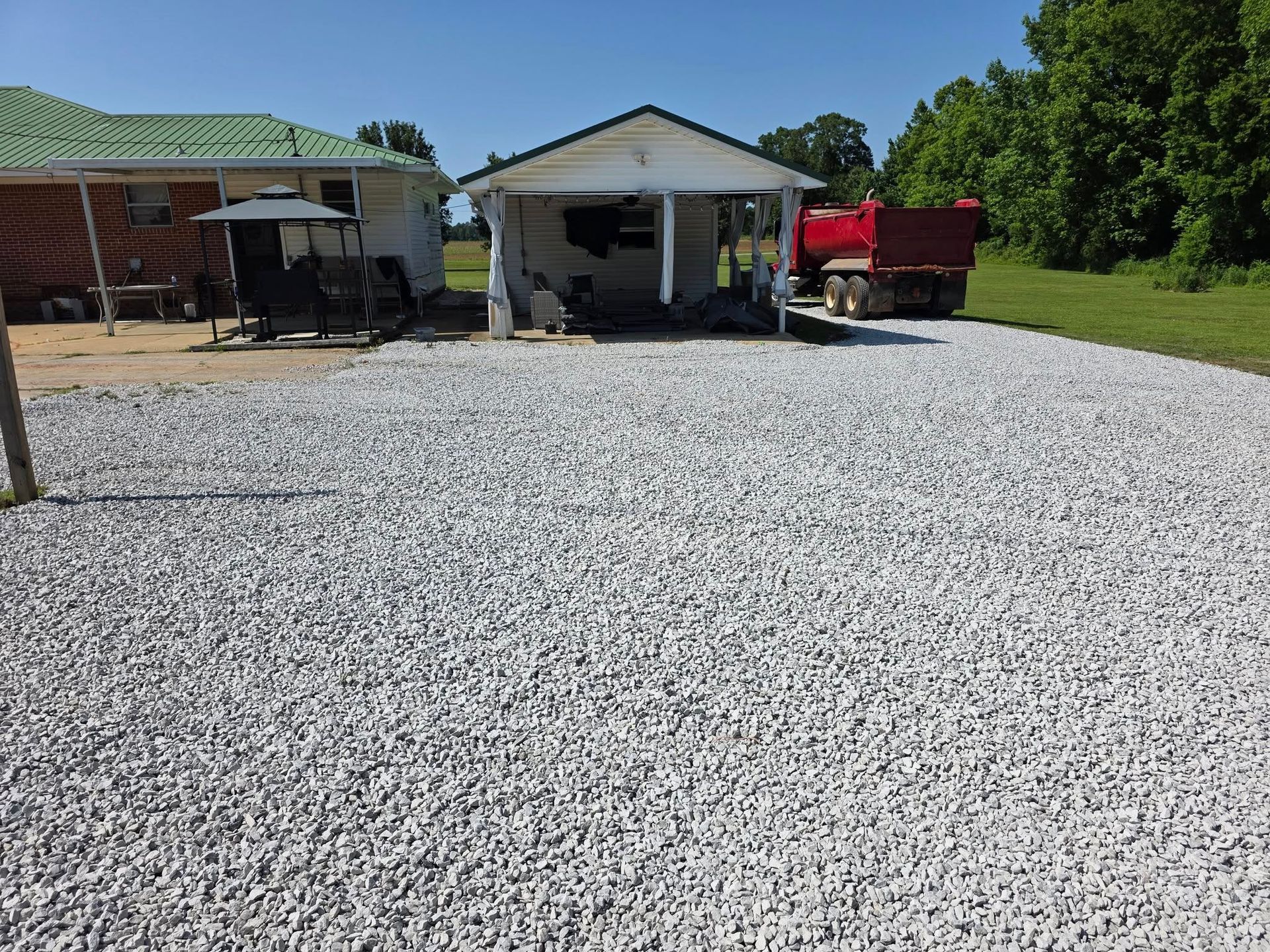 Gravel driveway in front of a small white building and red brick house on a sunny day.