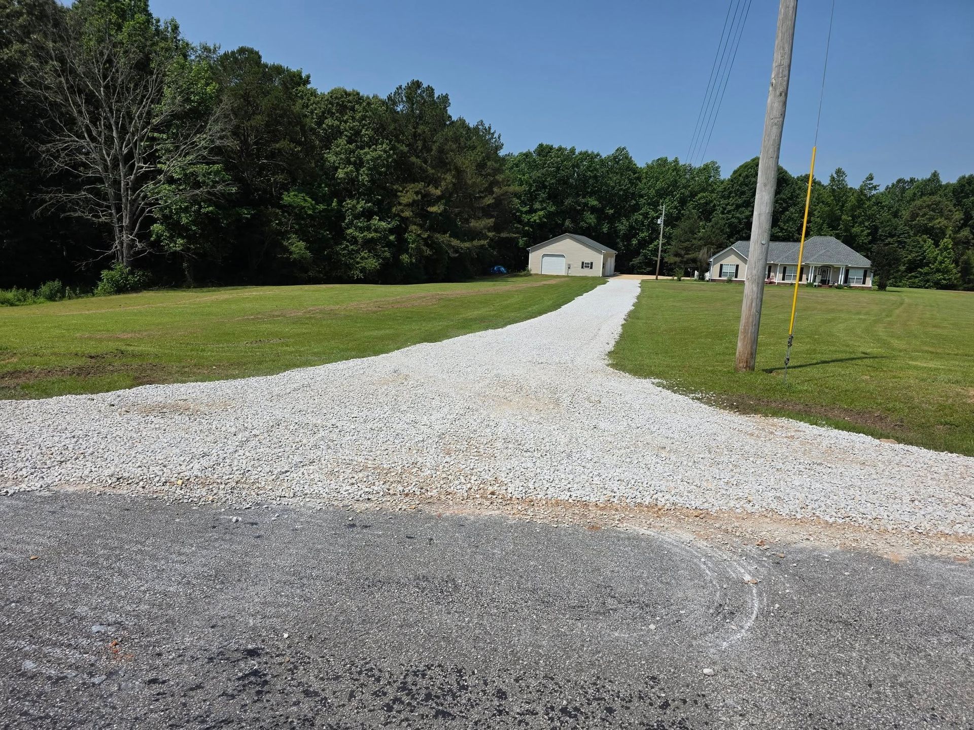 Gravel driveway splits into two, leading to a house and garage, with green grass and trees.