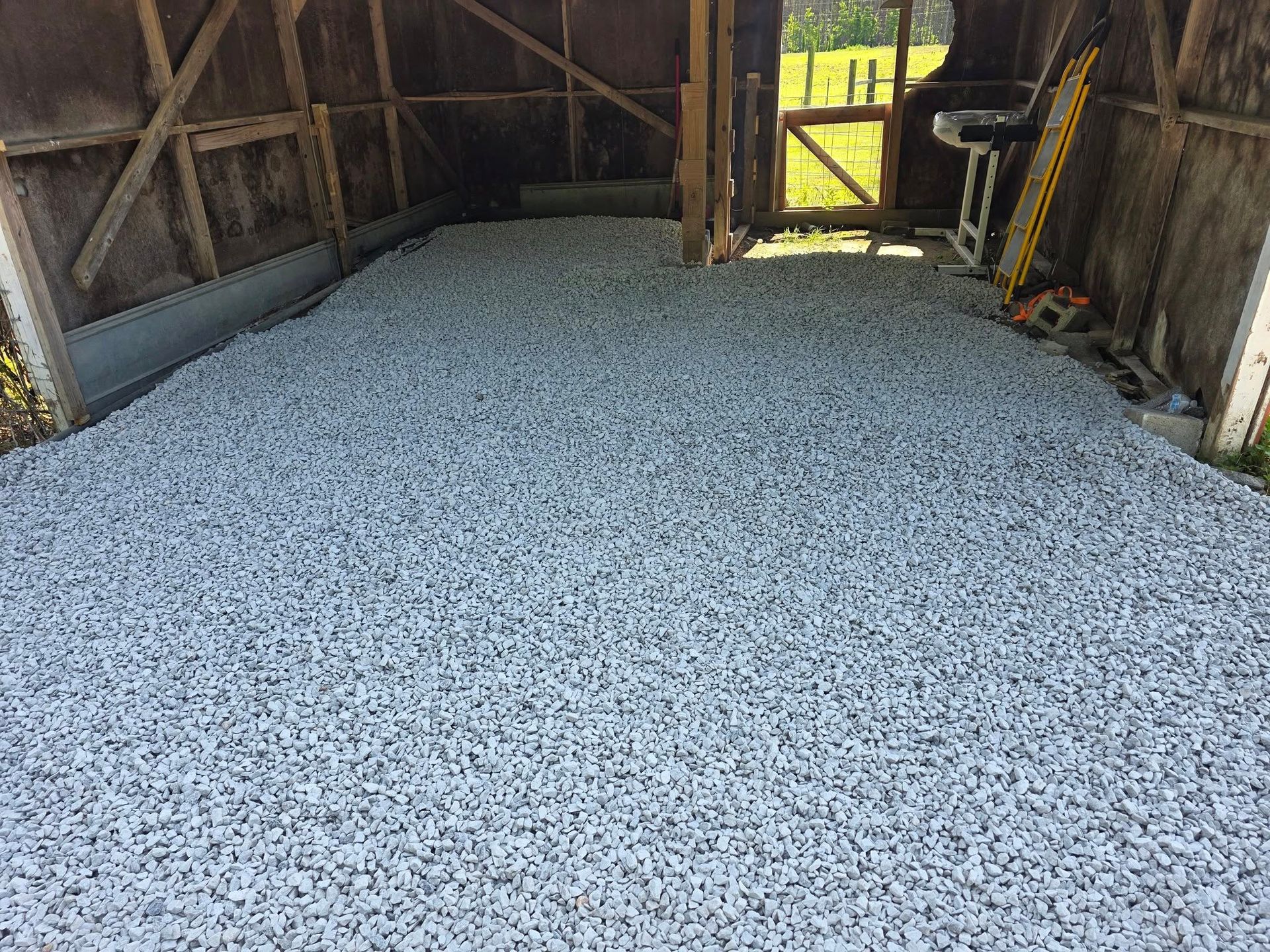 Gravel floor inside a wooden shed. Sunlight streams through the doorway.