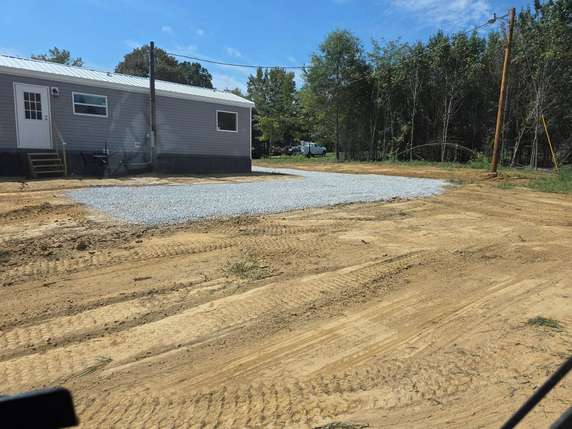 A gravel driveway next to a grey building, on a dirt and sand lot.