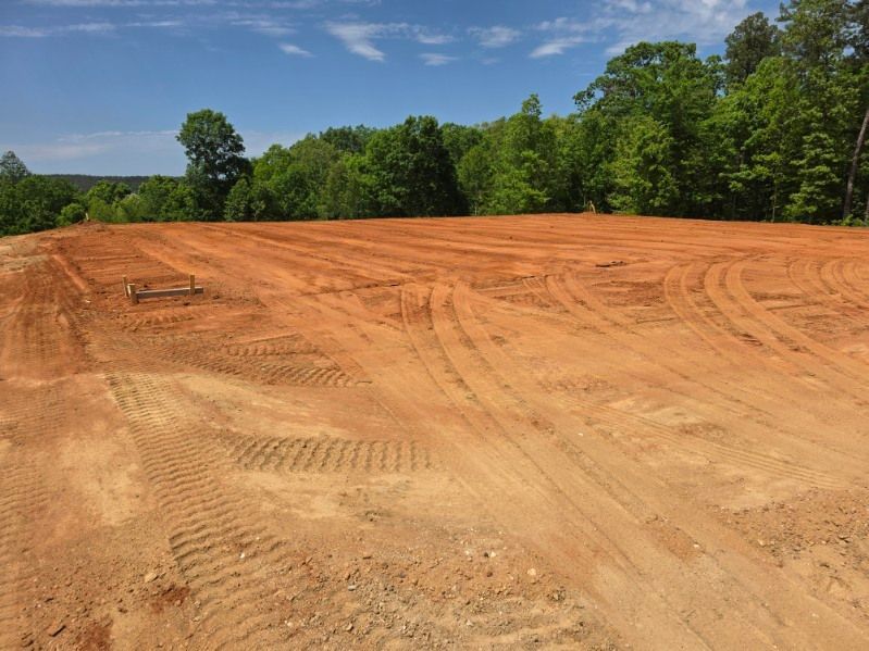 Cleared red dirt lot under a blue sky, bordered by green trees
