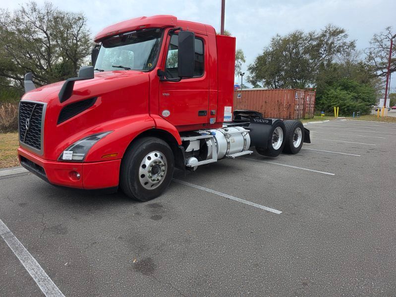 Red semi-truck parked in an empty lot, viewed from the front-left side.