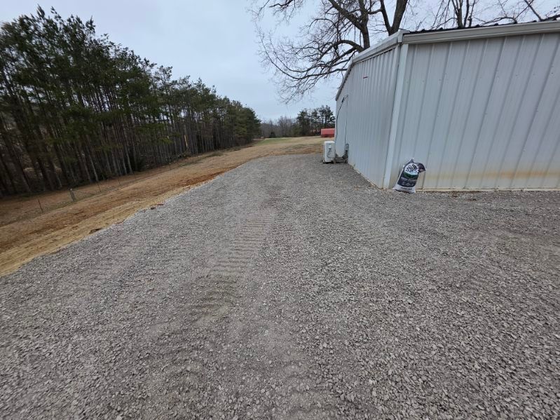 Gravel driveway next to a white building and a row of trees on a cloudy day.