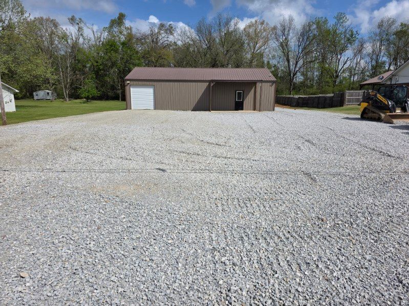 Gravel lot with a tan garage building under a partly cloudy sky, construction equipment at right
