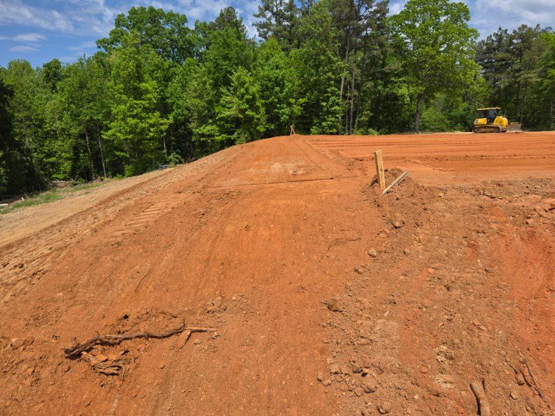 Dirt embankment on a construction site with trees in the background and a yellow bulldozer on the ridge