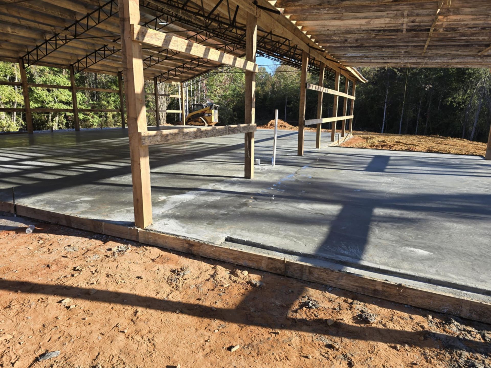 Concrete floor of a building under construction with wooden beams and supports in an outdoor setting.
