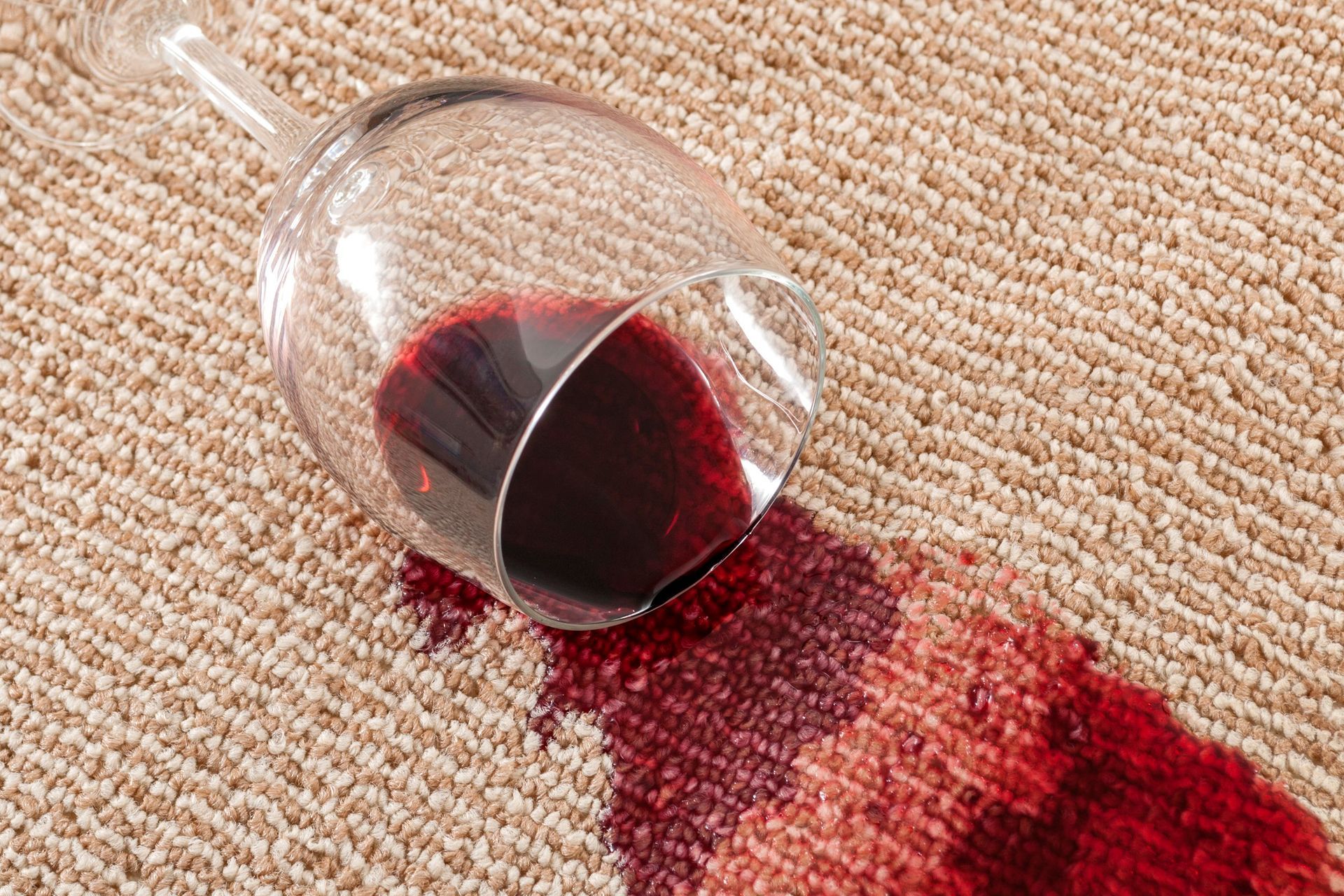 A glass of red wine spilled on a carpet.
