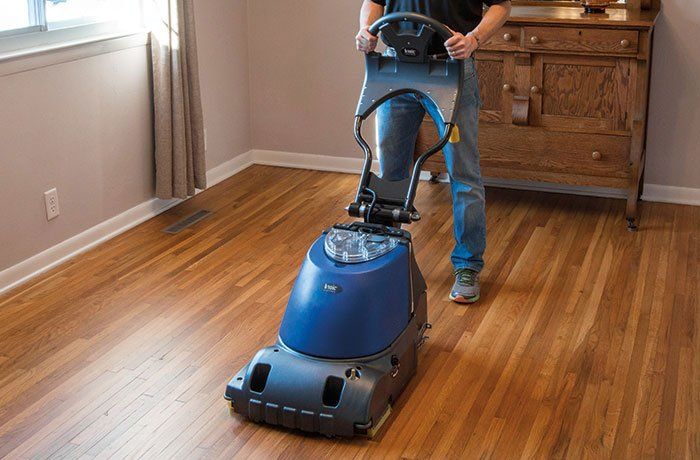 A man is using a machine to clean a wooden floor.