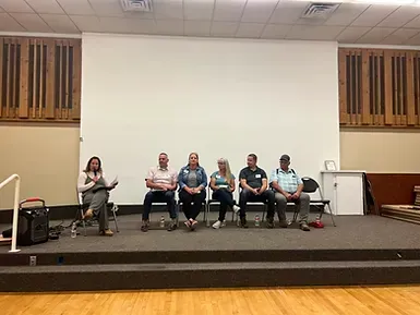 A group of people are sitting on a stage in front of a large screen.