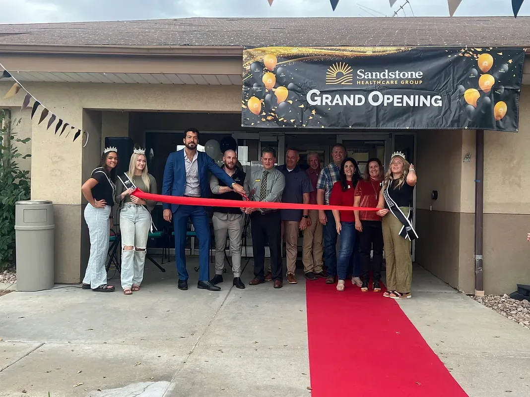 A group of people are standing in front of a building holding a red ribbon.