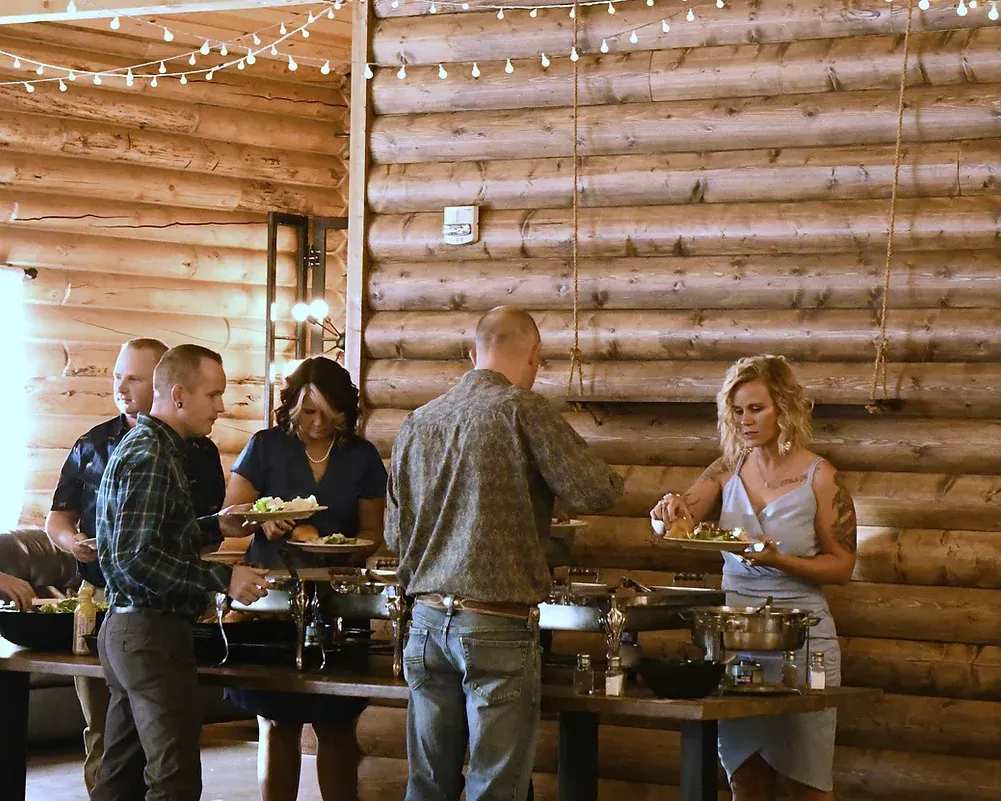 A group of people are standing around a buffet table in a log cabin.
