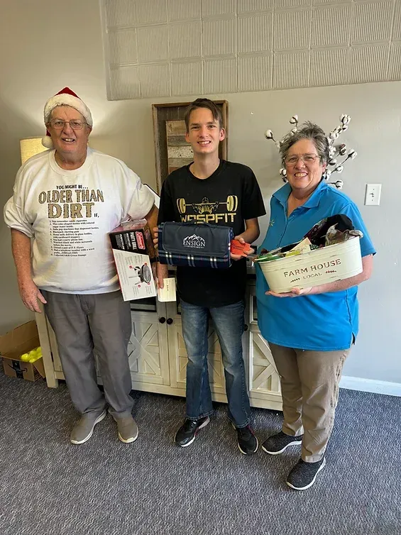 Three people are standing next to each other in a living room holding gifts.