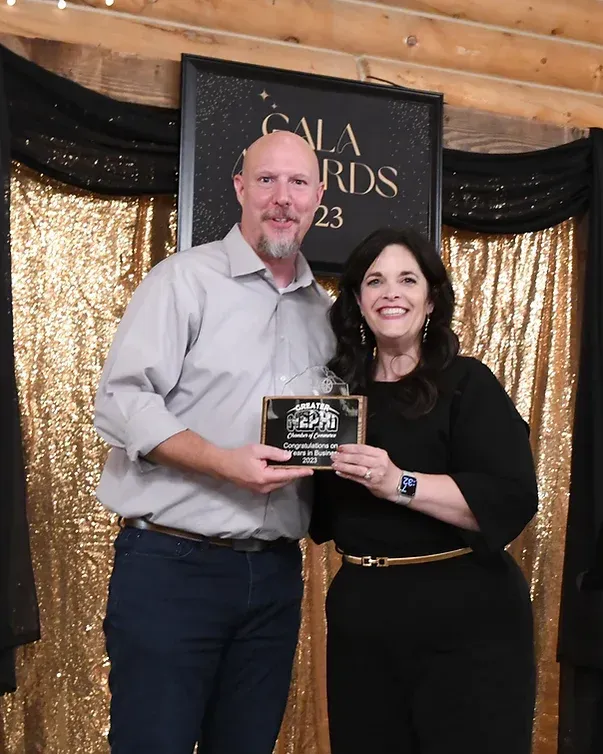 A man and woman are posing for a picture in front of a gala awards sign