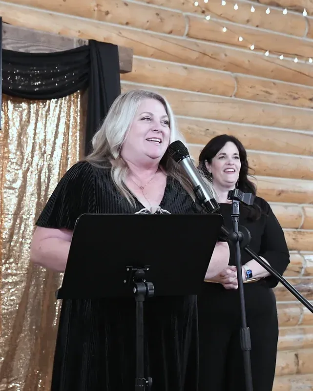 Two women are standing at a podium speaking into microphones.