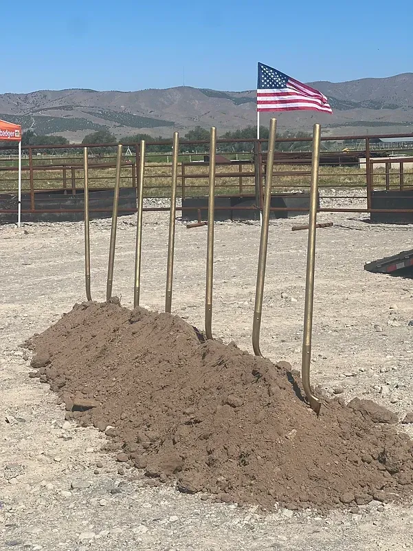A pile of dirt is sitting next to a row of wooden poles with an american flag flying in the background.