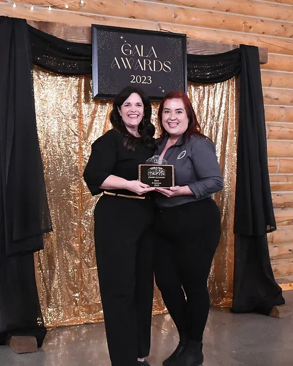 Two women are posing for a picture in front of a gala awards sign.
