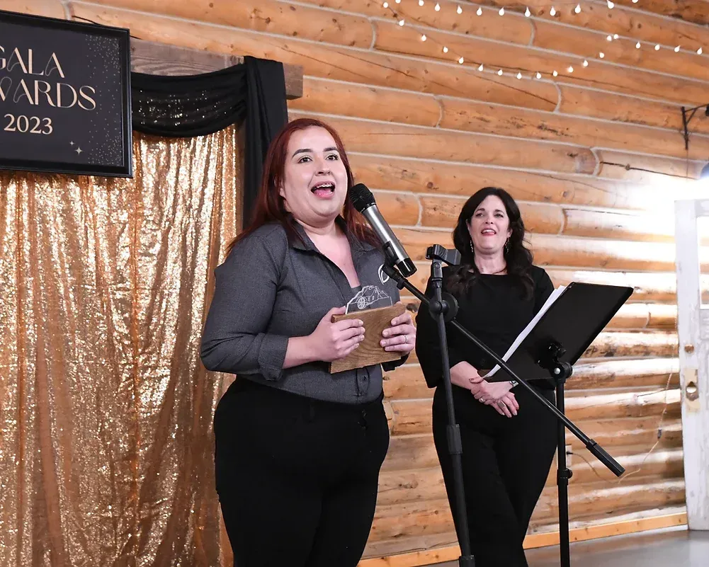 Two women are singing into microphones in front of a sign that says gala awards.