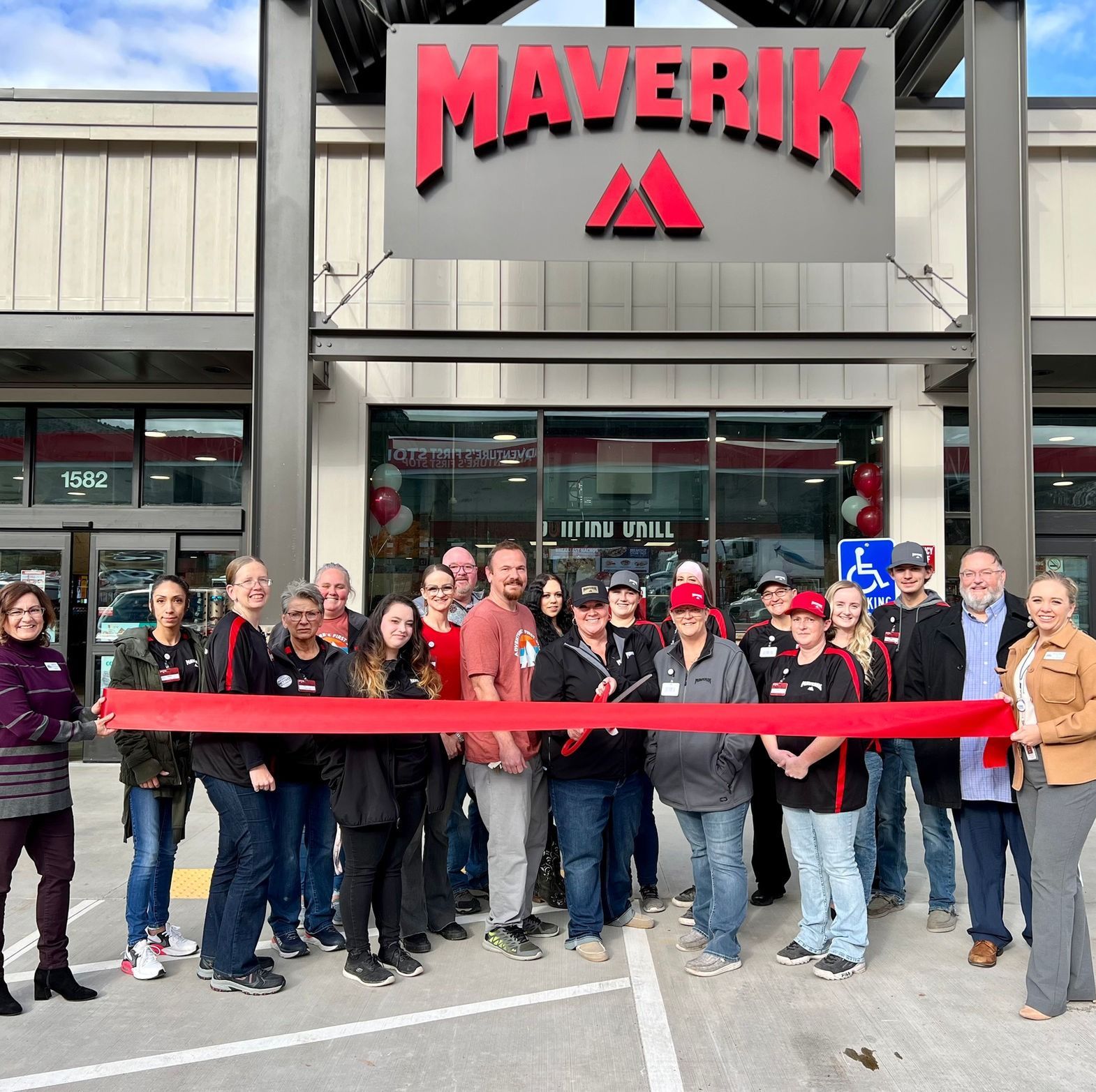 A group of people holding a red ribbon in front of a maverick store