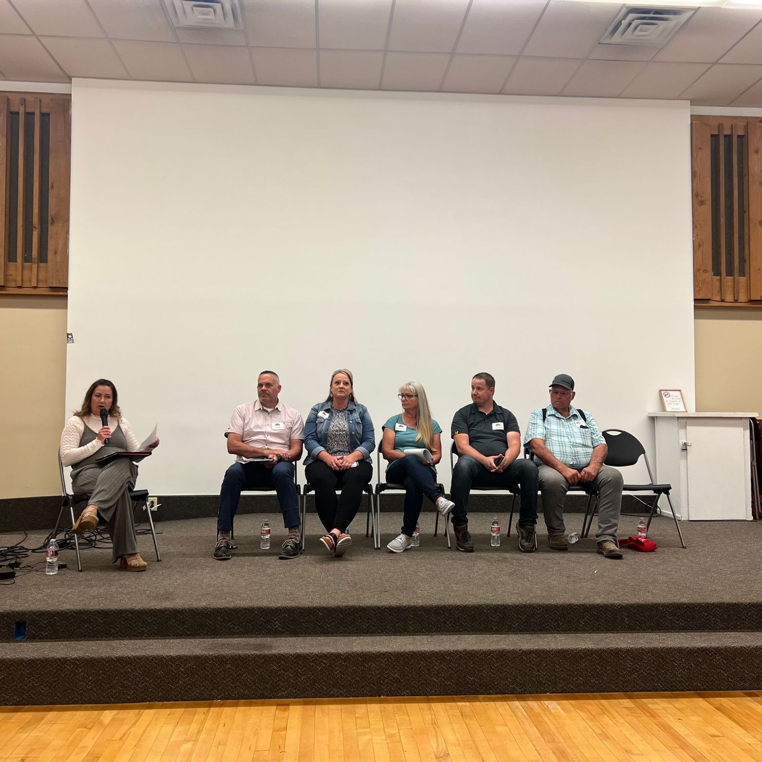 A group of people are sitting on a stage in front of a large screen.