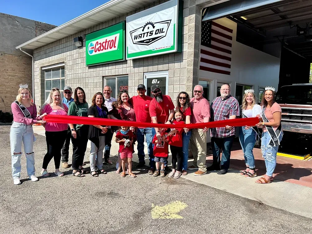 A group of people are standing in front of a building holding a red ribbon.