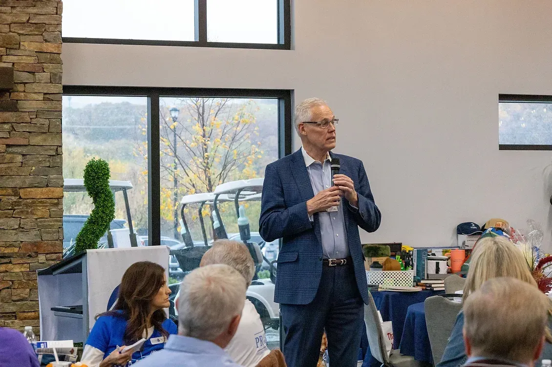 A man in a suit is standing in front of a group of people holding a microphone.