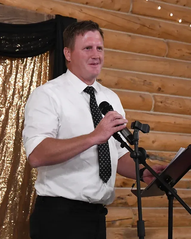A man in a white shirt and tie is speaking into a microphone