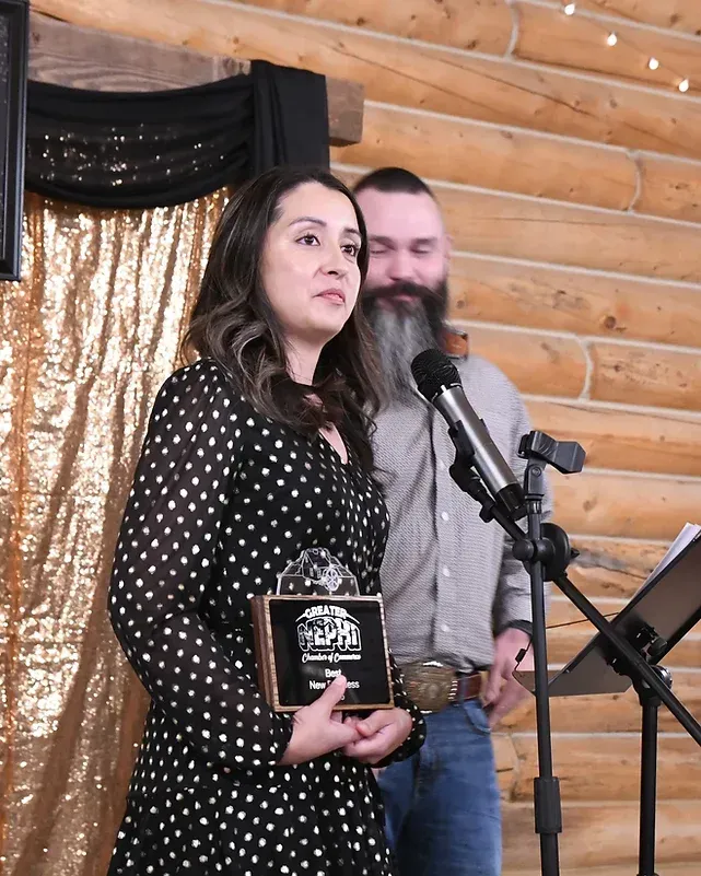 A woman in a polka dot dress is holding an award in front of a man with a beard