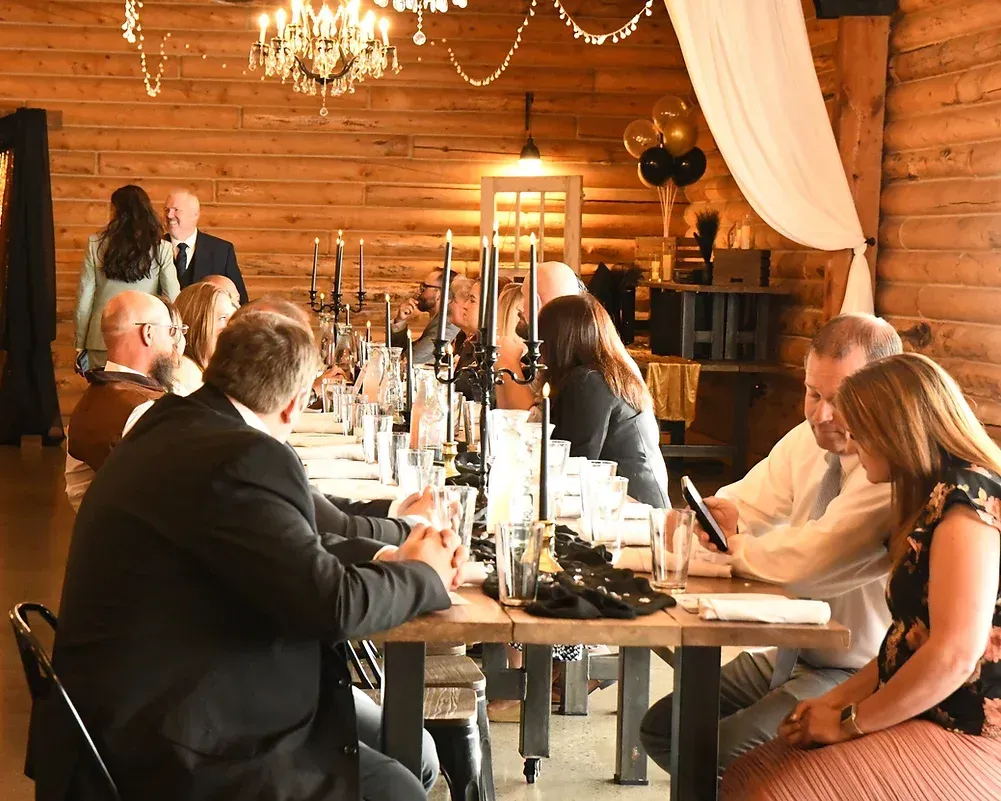 A group of people are sitting at long tables in a wooden room.