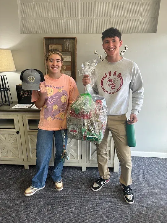 A man and a woman are standing next to each other in a living room holding bags of candy.