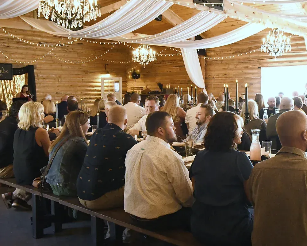 A large group of people are sitting at long tables in a large room.