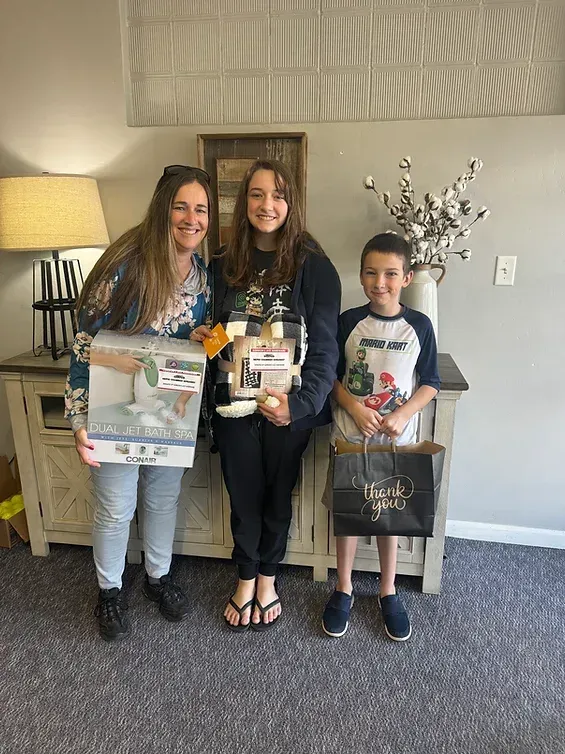 Three people are standing next to each other in a living room holding gifts.