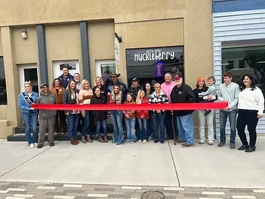 A group of people are standing in front of a building holding a red ribbon.