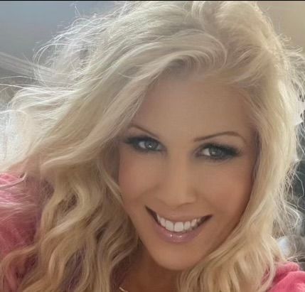 A woman is sitting in a chair with her arms crossed and smiling.