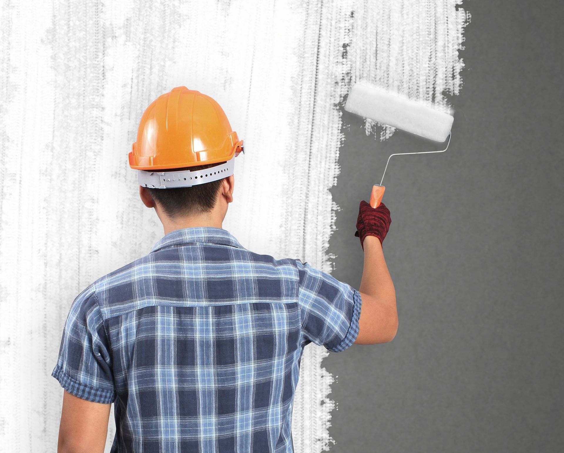 Un uomo che indossa un casco sta dipingendo un muro con un rullo.