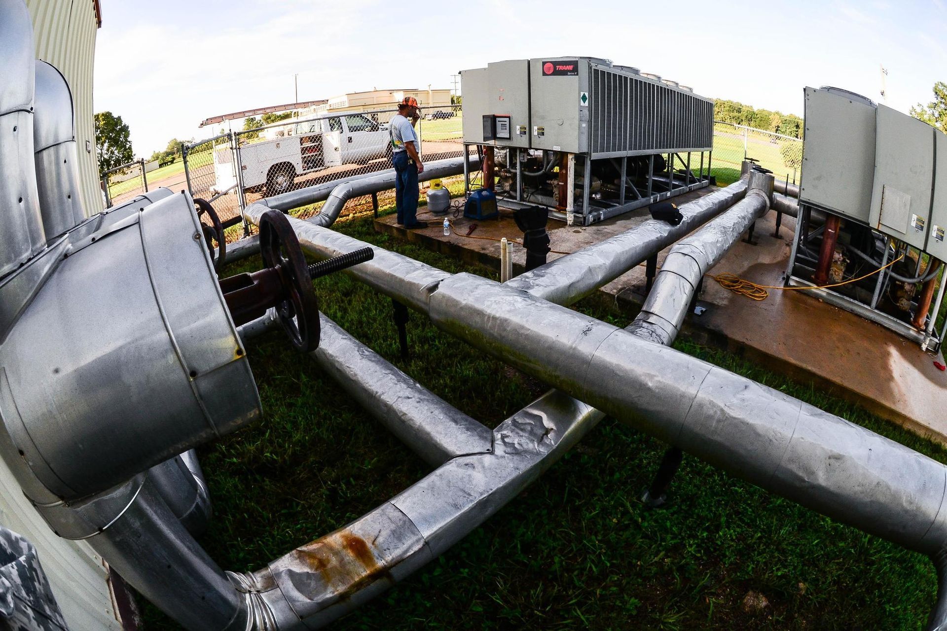 A man is standing in front of a large machine surrounded by pipes.