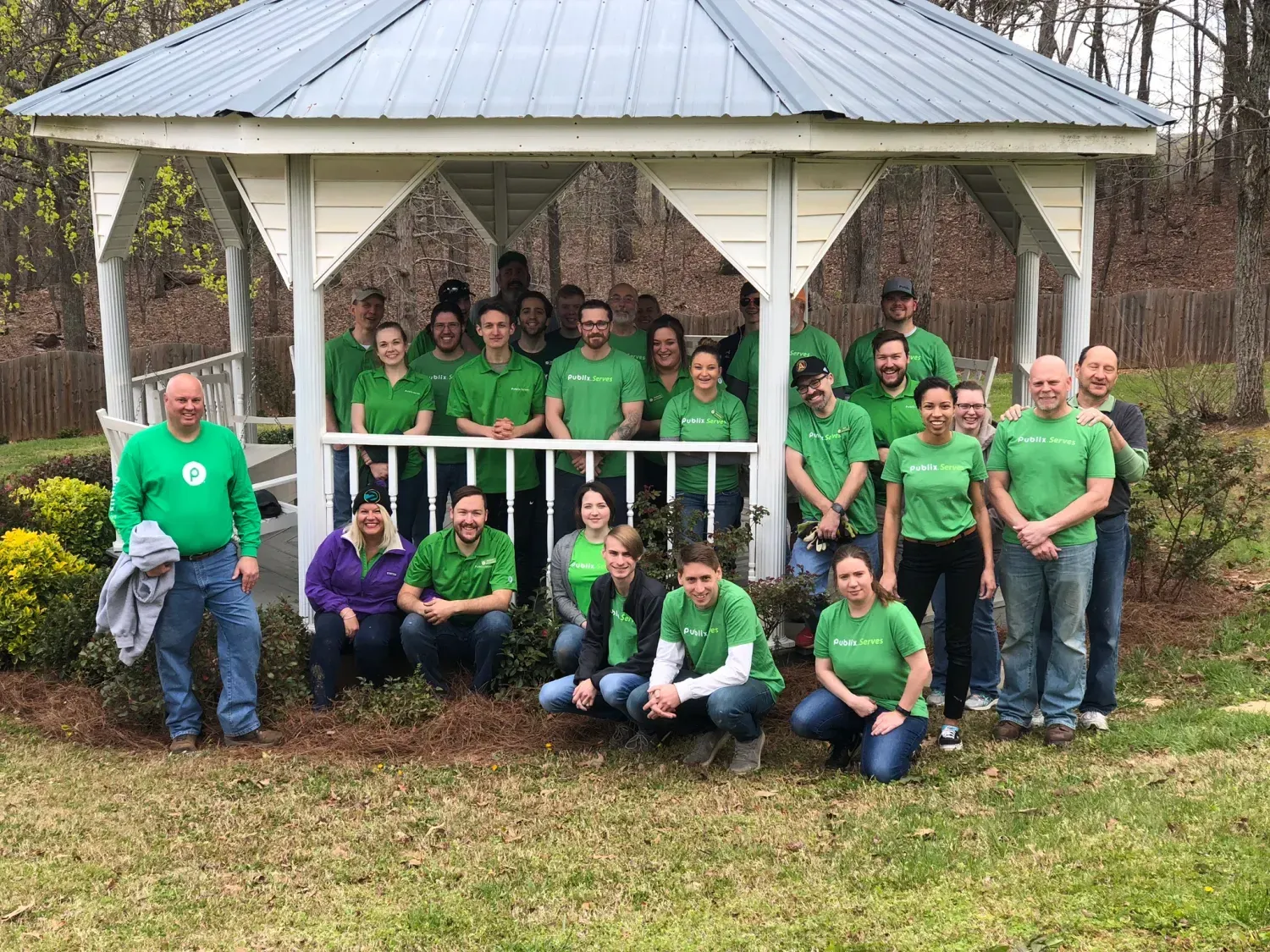 A group of people in green shirts are posing for a picture in front of a gazebo.