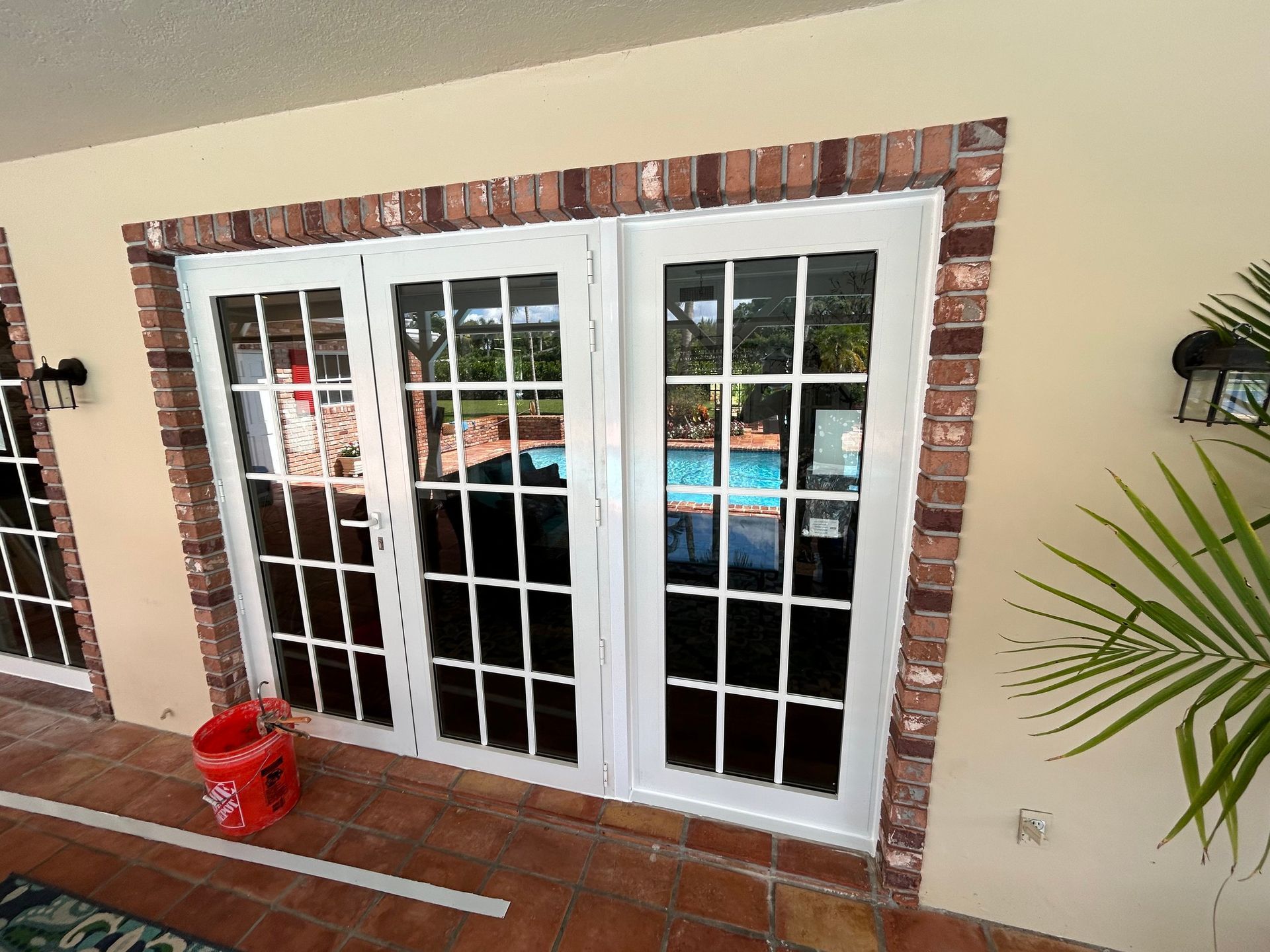 A red bucket sits on a patio next to a french door