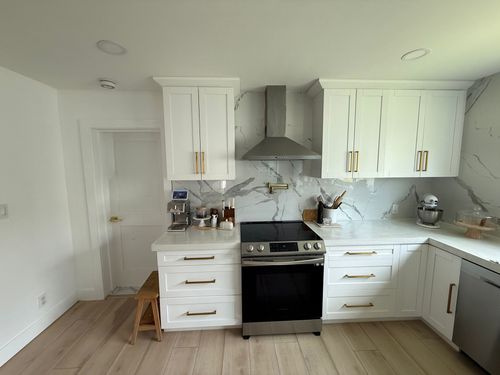 White remodeled kitchen with marble backsplash and stainless steel appliances; light wood floors.