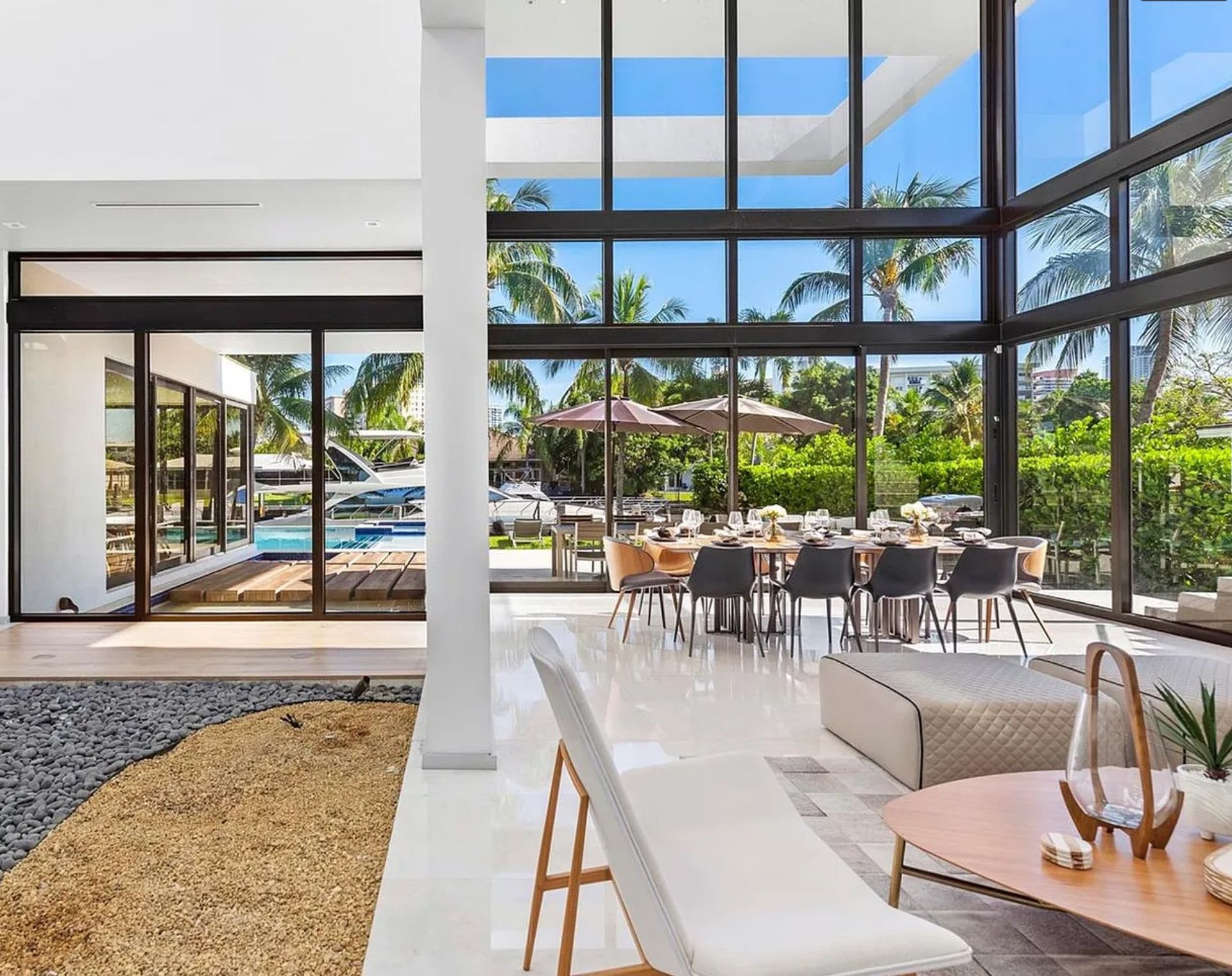 A living room with a lot of windows and a dining room with tables and chairs.