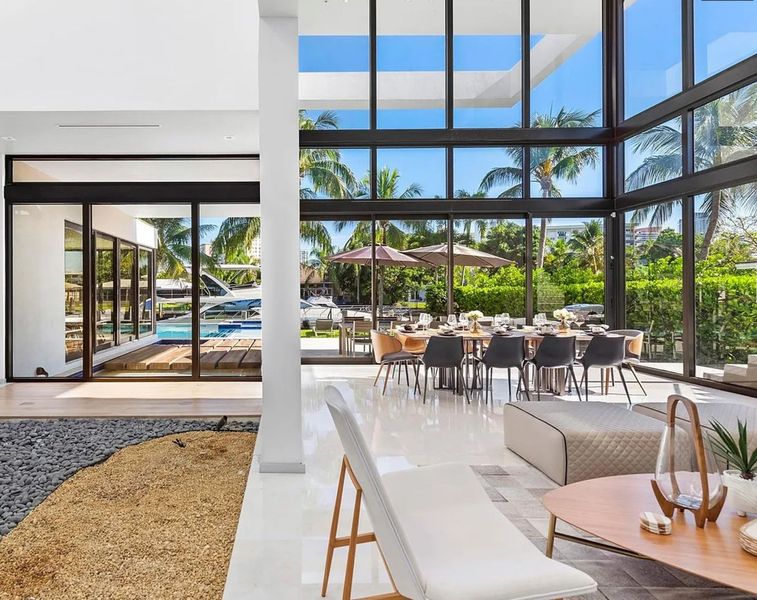 A living room with a lot of windows and a dining room with tables and chairs.