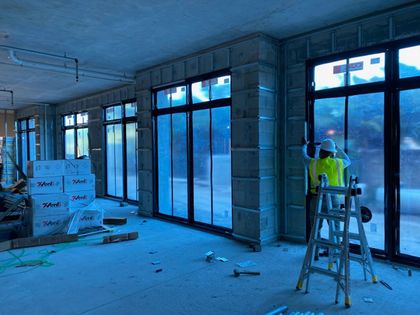 A man is standing on a ladder in a room with a lot of windows.