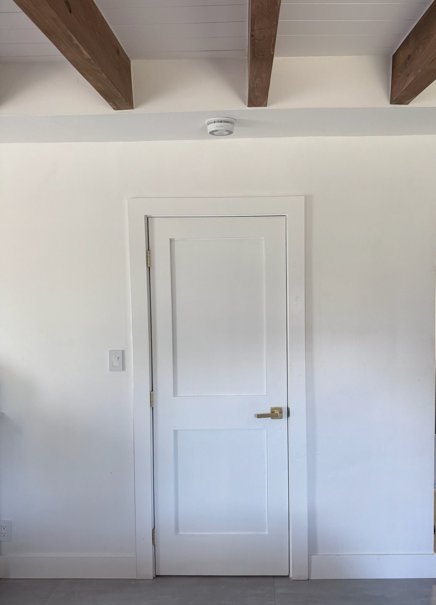 A white door in a room with wooden beams on the ceiling.