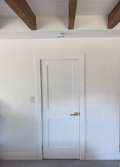 A white door in a room with wooden beams on the ceiling.